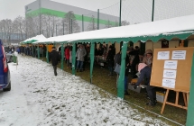 stoiska pod namiotami, przy nich duza grua osob ,w tle padajacy snieg