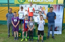Troje chłopców na podium. Obok nich inni uczestnicy konkurencji sportowej. 