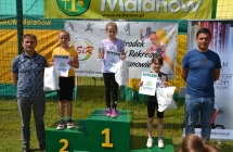 Trzy dziewczynki z nagrodami na podium. Obok dwoje mężczyzn 