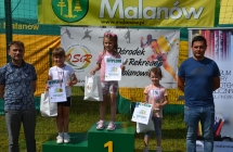 Trzy uśmiechnięte dziewczynki na podium. Obok dwaj szczęśliwi mężczyźni 