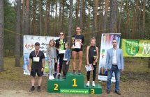 Trzy dziewczyny na podium, dwoje mężczyzn obok 