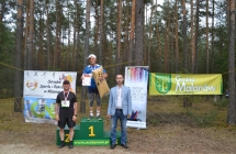 Starszy mężczyzna na podium, trzyma medal oraz dyplom i nagrodę, obok niego dwaj mężczyźni