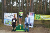 Uśmiechnięta kobieta na podium zawodów, obok niej dwaj mężczyźni 
