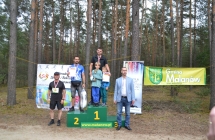 Dwoje mężczyzn na podium, jednemu z nich towarzyszy dwójka chłopców. Obok podium dwoje mężczyzn 