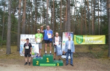 Pięcioro mężczyzn, trojka z nich stoi na podium, zawodnik na pierwszym miejscu trzyma w górze puchar 
