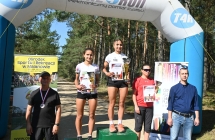 Trzy kobiety na podium. Obok nich stoi dwoje mężczyzn 