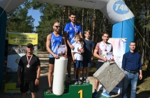 Zwycięzcy na podium. Stoją z nagrodami. Obok mężczyźni 
