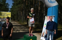 Kobieta na podium. Obok dwoje mężczyzn 